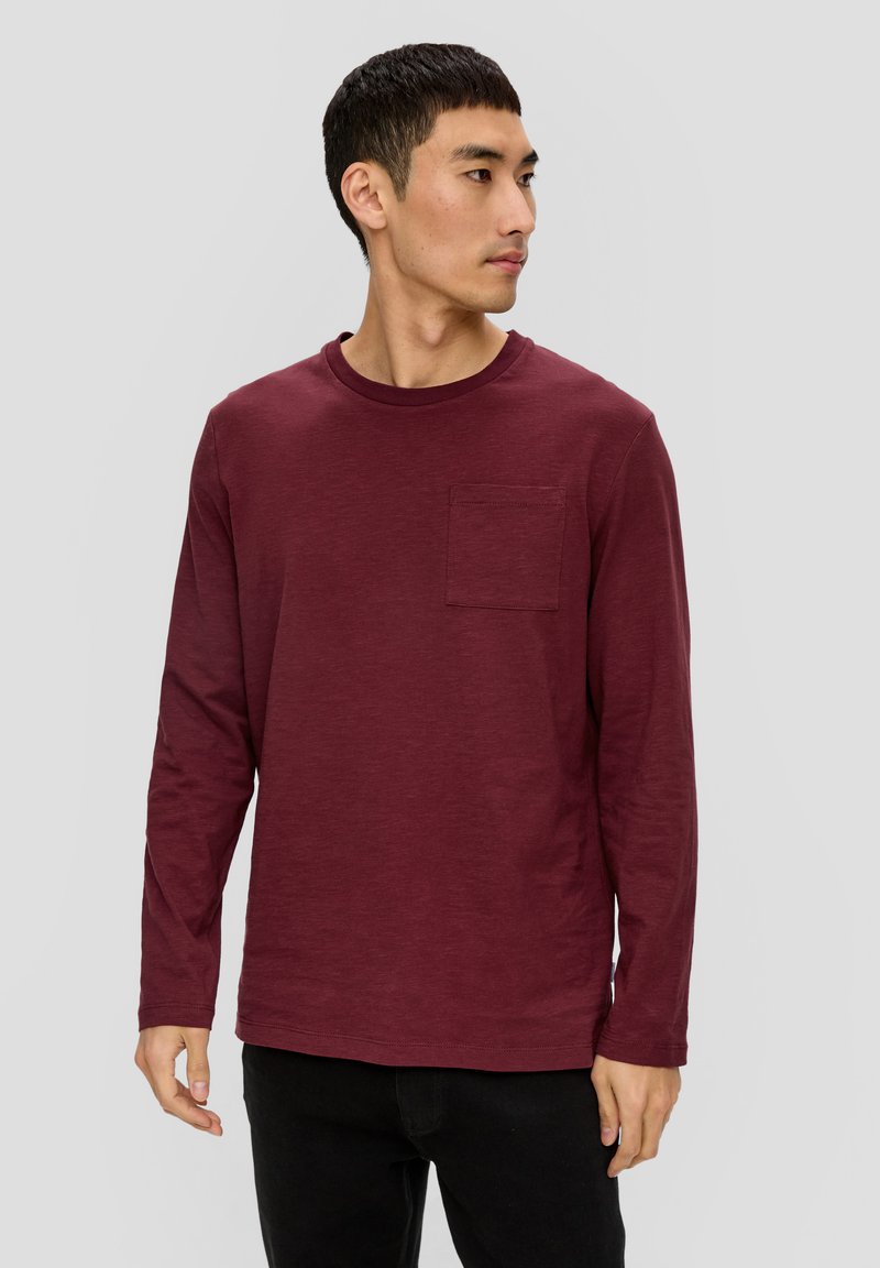 Bordowa koszula z długim rękawem, uszyta z miękkiego materiału, z okrągłym dekoltem i kieszonką na lewej piersi, w zestawie z czarnymi spodniami.