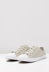 Baskets en toile gris clair avec œillets dorés, bout arrondi blanc et semelle en caoutchouc plate blanche. Design à lacets avec accents texturés.