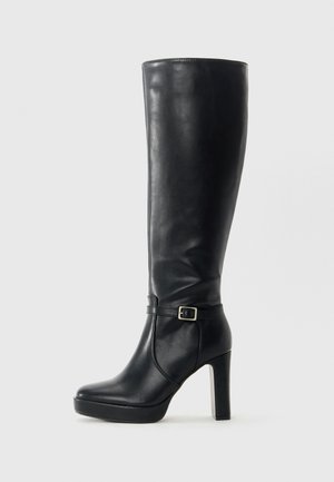 Botte en cuir noire montante jusqu'au genou avec un talon épais et haut et une petite sangle à boucle autour de la cheville, présentée sur un fond clair uni.