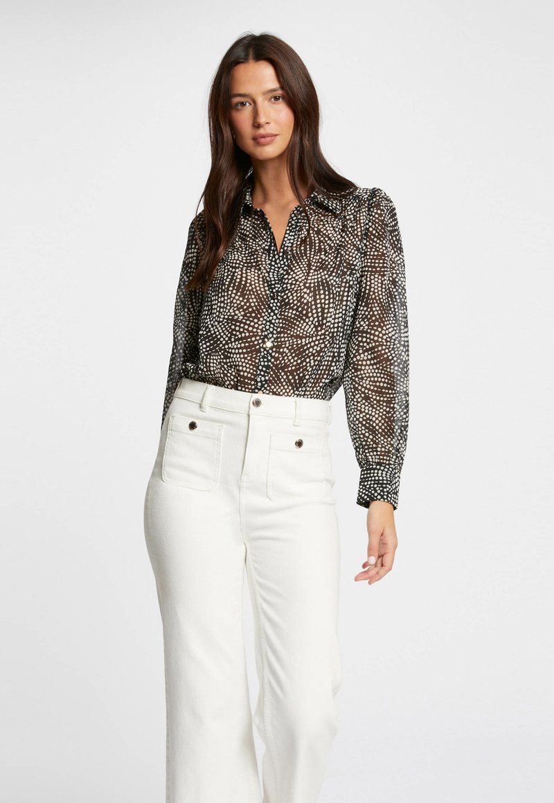 Zwart-witte geblokte blouse met een kraag, knoopsluiting aan de voorkant en lange mouwen, gecombineerd met hoge witte wijde pijpen broek.