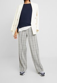 Vit dubbelknäppt blazer, marinblå topp och grårutiga vida byxor. Sneakers har en blå och vit design med texturerade detaljer.