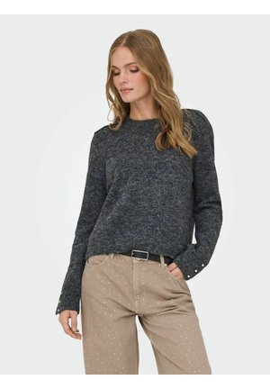 Dark grey knitted sweater with long sleeves, featuring a round neckline and button details on the cuffs, paired with light beige polka dot pants.