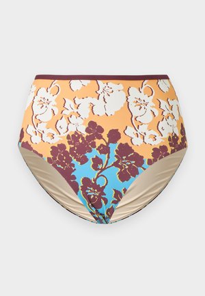 Mujer de pie descalza con las manos en las caderas, con top de bikini marrón tipo halter y braguitas de bikini de talle alto con estampado floral sobre fondo blanco.