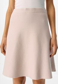 Jupe rose clair en tissu doux et texturé ; design évasé avec une taille lisse, longueur genoux et une silhouette légèrement évasée.