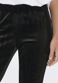 Pantaloni in velluto nero con una texture liscia e un design aderente. La cintura è elastica, con una cucitura laterale e una leggera lucentezza.