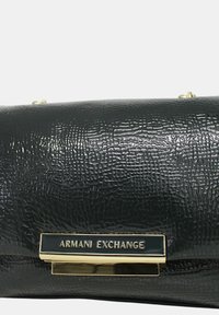 Borsa a tracolla nera con finitura lucida, con un emblema dorato etichettato "Armani Exchange" su un elegante dettaglio orizzontale.