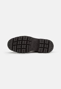 Semelle de botte en caoutchouc noir avec des crampons profonds, présentant des rainures horizontales et verticales pour l'adhérence, et une finition texturée pour la prise.