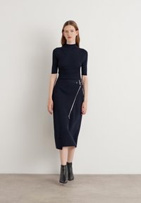 Haut en maille marine à manches courtes associé à une jupe taille haute avec une fermeture éclair diagonale et un détail de ceinture, complété par des bottines noires.