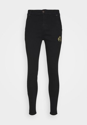 Jeans skinny de mezclilla negra con una textura suave, que presentan un logo bordado en dorado en la parte delantera, cintura alta y diseño de cinco bolsillos.