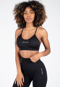 Sujetador deportivo negro con tirantes ajustables y logo, combinado con leggings negros de cintura alta que presentan un detalle de logo en el costado. Textura suave.