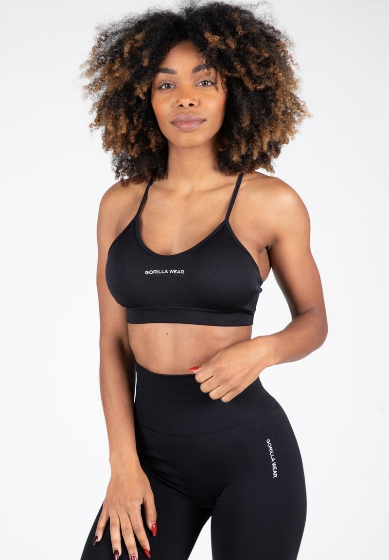 Sujetador deportivo negro con tirantes ajustables y logo, combinado con leggings negros de cintura alta que presentan un detalle de logo en el costado. Textura suave.