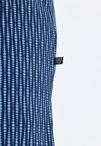 Tessuto blu navy con linee verticali di punti azzurri, con un'etichetta nera visibile sul bordo sinistro. La superficie sembra liscia.