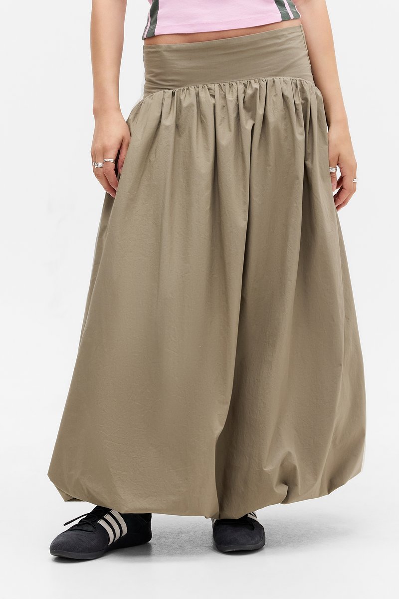 Gonna khaki a vita alta con texture arricciata, caratterizzata da una cintura larga e una silhouette fluida. Abbinata a scarpe nere.