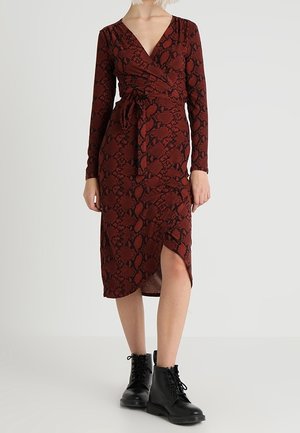 Czerwona kopertowa sukienka w wężowy wzór z długimi rękawami, głębokim dekoltem w serek, wiązaniem z boku i rozcięciem do kolan, połączona z czarnymi botkami na sznurowadła.