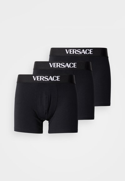 Trois paires de boxers noirs en tissu doux et extensible. Chaque modèle présente une ceinture noire avec le logo "VERSACE" en blanc.