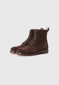 Stivali in suede marrone con punta rotonda, lacci frontali e occhielli in metallo. Presentano un tacco in pelle impilato e linguette per una facile calzata.