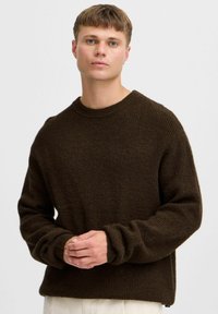 Donkerbruin gebreid sweater met een ronde hals, lange mouwen en geribbelde textuur. Beschikt over een relaxte pasvorm en een laag ingezette schouderontwerp.