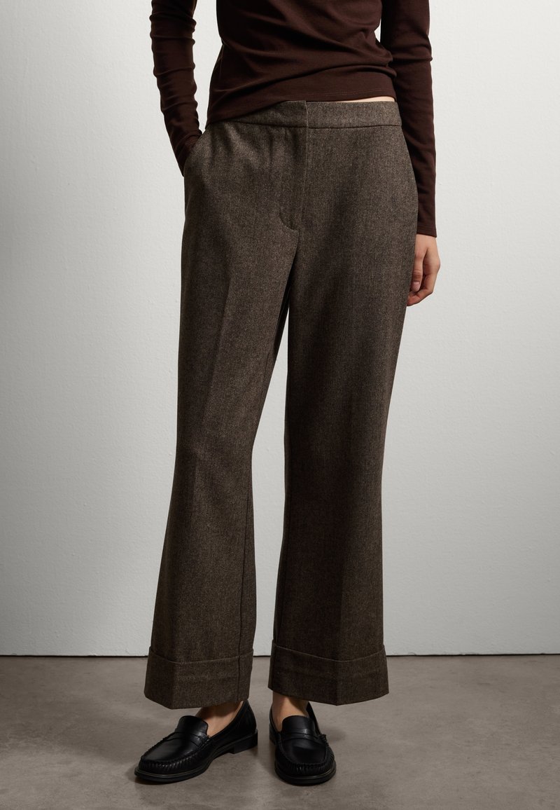 Bruine, gestructureerde, brede broek met een omgeslagen zoom en zakken aan de voorkant, gecombineerd met zwarte loafers en een aansluitend bruin topje.