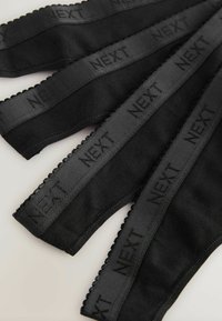 Svarta elastiska band med vågiga kanter och tryckta logotyper, arrangerade i ett platt mönster som visar en jämn yta och enhetlig bredd.