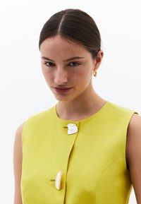 Abito giallo senza maniche con una fibbia in argento texture e un dettaglio a spillo giallo liscio. Design semplice e tessuto con una leggera lucentezza.