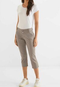 Ljust grå cropped byxor med två framskbuttons, sidoficka med dragkedja och kontrastsöm, matchade med en vit t-shirt med kort ärm och sneakers.