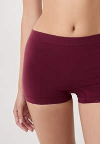 Shorts en coton bourgogne avec une taille et un ourlet sans couture. Texture douce, design taille mi-haute et silhouette ajustée. Aucun motif visible ni embellissements.
