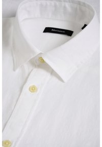 Chemise blanche boutonnée avec un col pointu et des boutons couleur crème, montrant une partie de l'avant et de la zone du col.