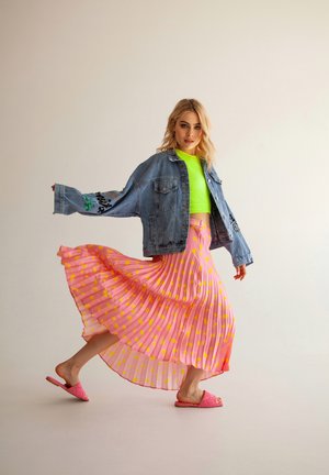 Farkkutakki brodeeratulla yksityiskohdalla, neonvihreä crop-top, vaaleanpunainen hame muotona, jossa keltaisia pisteitä, ja vaaleanpunaiset liukusandaalit.
