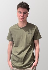 T-shirt in cotone verde oliva con maniche corte e scollatura rotonda, con il logo nero "CALVIN KLEIN" sul lato sinistro del petto.