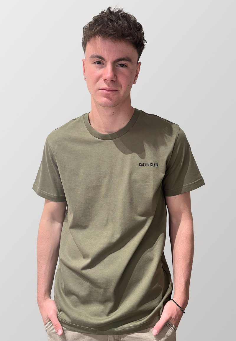 T-shirt in cotone verde oliva con maniche corte e scollatura rotonda, con il logo nero "CALVIN KLEIN" sul lato sinistro del petto.