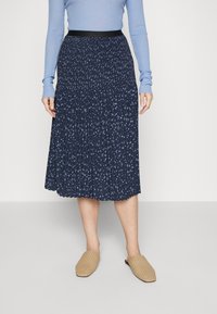 Námořnická plisovaná sukně s malými bílými květinovými vzory, vybavená černým pasem. Nosí se s tkanými béžovými nazouvacími botami.