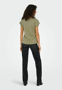 Olivenfarvet t-shirt med korte �ærmer og rund halsudskæring, parret med højtsiddende sorte jeans og sko med blokhæle, set fra ryggen.