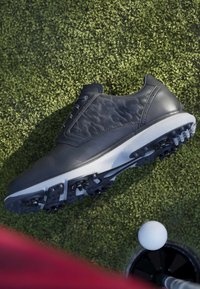 Chaussure de golf sur gazon artificiel près d’une balle de golf placée au-dessus d’un trou sur un green.