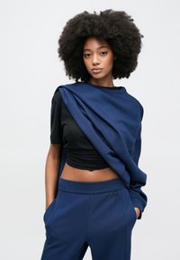 Μπλε ναυτικό φούτερ που κρέμεται πάνω από μαύρο κοντό τοπ, συνδυασμένο με μπλε ναυτικό παντελόνι τζόγκινγκ. Απαλό ύφασμα με άνετη εφαρμογή και πλαϊνές τσέπες.