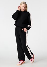 Ensemble sweat-shirt et pantalon de survêtement noirs avec des bandes latérales roses et blanches, fabriqué en tissu doux, présentant une coupe décontractée et une taille élastique.