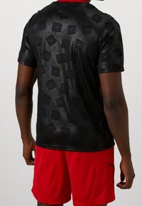 Musta urheilupaita, jossa on teksturoitu neliökuvio, lyhyet hihat ja pyöreä kaula-aukko, yhdistetty punaisiin shortseihin, joissa on sivutasku.