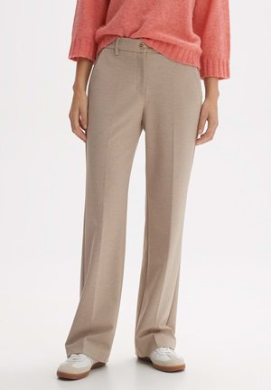Pantalons beige à jambes larges en tissu lisse et texturé. Présentent une fermeture à bouton devant et des poches. Portés avec des baskets blanches.