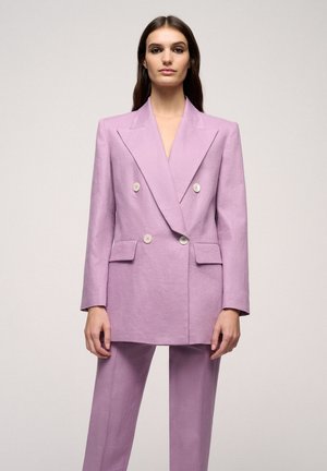 Dubbelzijdige blazer in licht lavendelstof met scherpe revers, voorzakken en witte knopen; gecombineerd met bijpassende broek.