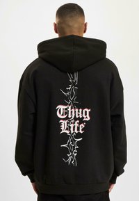 Sudadera negra con un gran gráfico en blanco y rojo que dice "Thug Life" en la parte posterior. Cuenta con una capucha con cordón y puños y dobladillo de canalé.