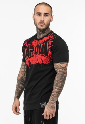 Melna īsām piedurknēm T-kreklā ar sarkano "TAPOUT" logotipu, kas rotāts ar šļakatu dizainu priekšpusē. Izgatavots no kokvilnas, brīvs piegriezums, birka apakšmalā.