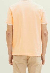 Kortärmad polotröja i ljusorange bomull med vita detaljer på kragen och ärmarna, med en avslappnad passform och sidoventiler.