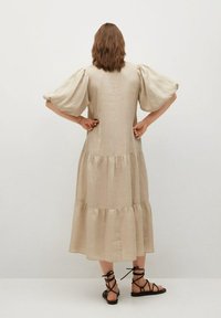 Beige pellavakleid, jossa on kerroksellinen muotoilu, lyhyet puffikuvat ja rento istuvuus. Ominaisuuksiin kuuluu polvimittainen helma ja sileä pinta.