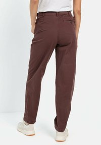 Maroon cotton pants with a relaxed fit, featuring side pockets and a back pocket, paired with light-colored sneakers.