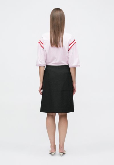 Ροζ τοπ με κοντά μανίκια και κόκκινες ρίγες, συνδυασμένο με μαύρη φούστα έως το γόνατο. Λείο ύφασμα και απλός σχεδιασμός. Τα τακούνια ολοκληρώνουν την εμφάνιση.