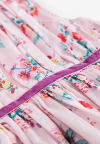 Gėlėta suknelė iš šviesiai rožinės medžiagos, puošta spalvingais gėlių raštais, klostėmis ir purpurinės aksominės juostos juosmens zonoje.