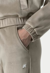 Tuta in pile beige con polsini e vita elasticizzati. Tasca visibile sul lato. Piccolo logo in accentatura vicino alla vita. Tessuto morbido.