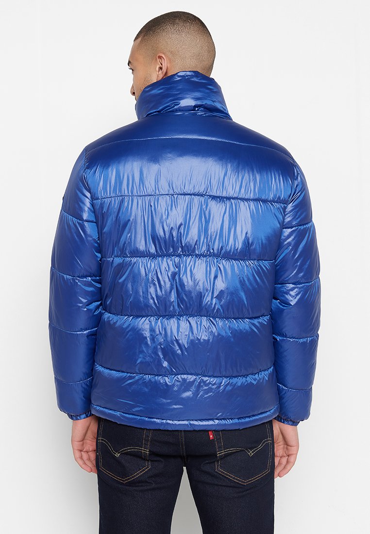 Blauer Daunenjacke mit hohem Kragen, gestepptem Design und glänzender Textur. Sie verfügt über lange Ärmel und einen Reißverschluss auf der Vorderseite.