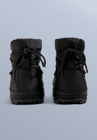 Mustat säänkestävät saappaat, joissa on pehmustettu yläosa, nauhakiinnitys ja kuvioitu kumipohja. Saappaissa on sileä viimeistely ja vahvistetut saumat.