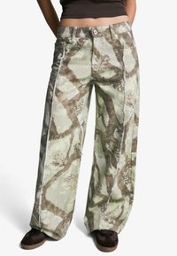 Hlače širokih nogavica u kamuflažnom uzorku, s nijansama zelene i smeđe boje, izrađene od izdržljivog materijala, s vidljivim šavovima i opuštenim krojem.