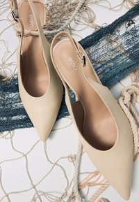 Béžové sandály na podpatku s špičatou špičkou, hladkou koženou texturou a minimalistickým designem. Logo embosované na vnitřní straně.